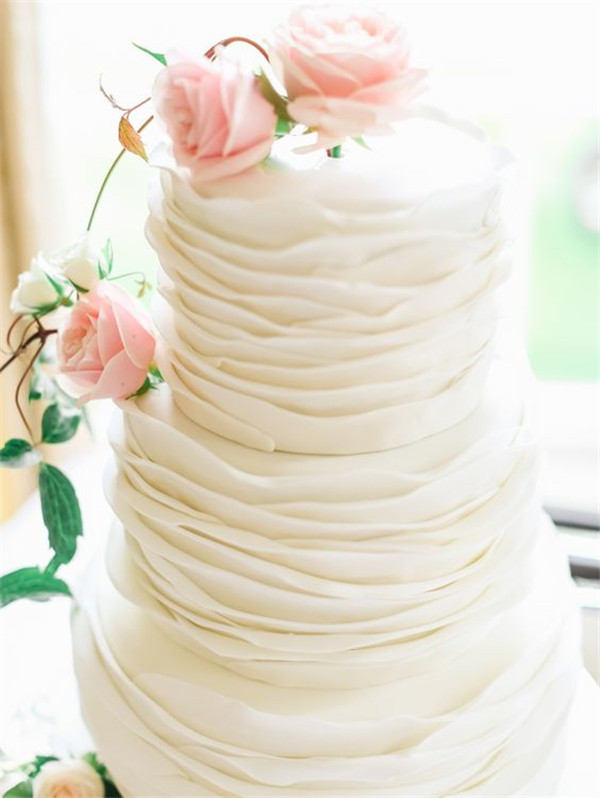 three tier white wedding cake decorated with fresh pink roses