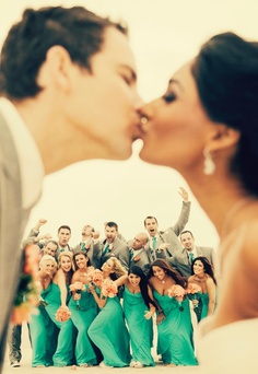 Cute shot of bride and groom kissing with wedding party behind them