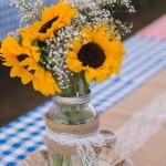 A picnic-themed reception table setting with burlap runners, and mason jar centerpieces with baby's breath and sunflowers!