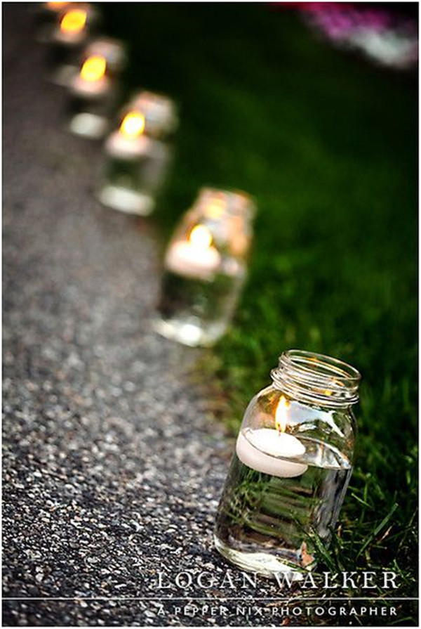 Mason jars with floating candles line the pathway to the backyard reception