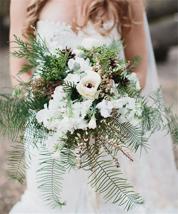 A rustic wedding bouquet with ferns, pieris, pinecones, and evergreens